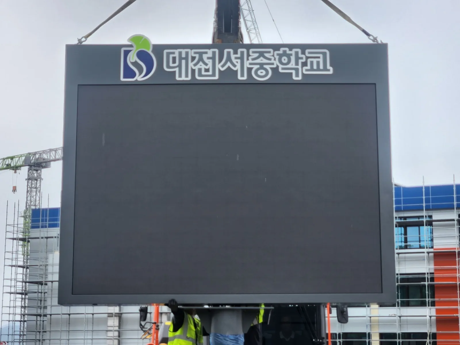 크레인으로 대전서중학교 로고가 새겨진 대형 지주형 전광판을 들어올려 설치하는 현장