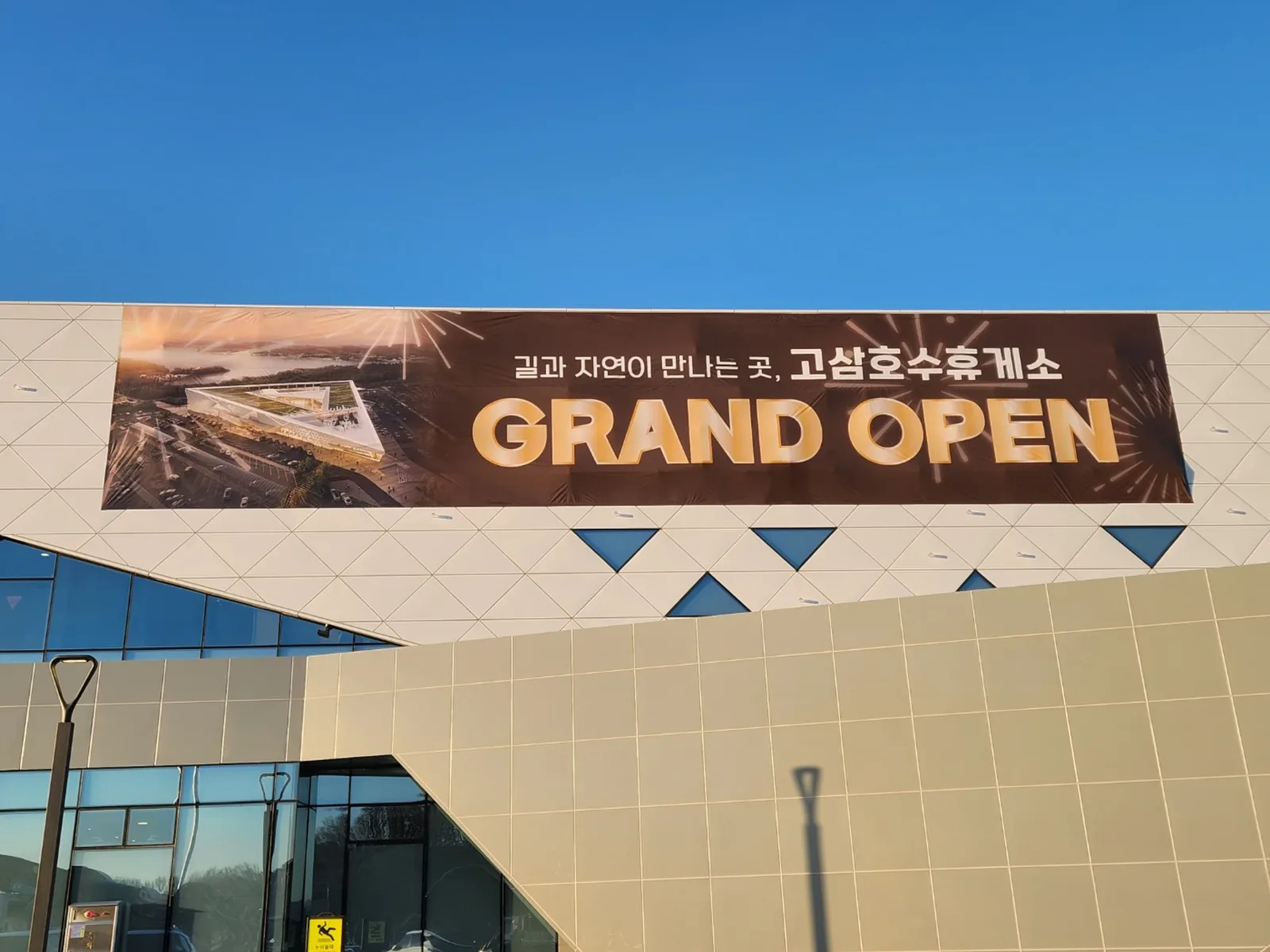 고속도로 휴게소 건물 외벽에 설치된 대형 그랜드오픈 홍보 배너