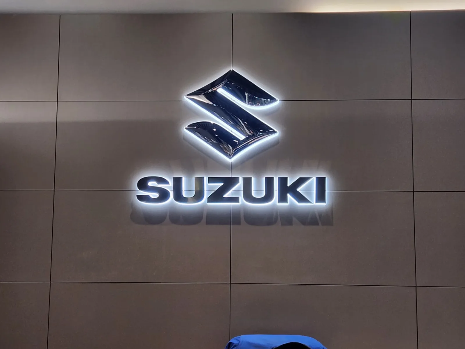 실내 벽면에 설치된 SUZUKI 로고 백라이트 채널사인 근접 사진, 점등 상태