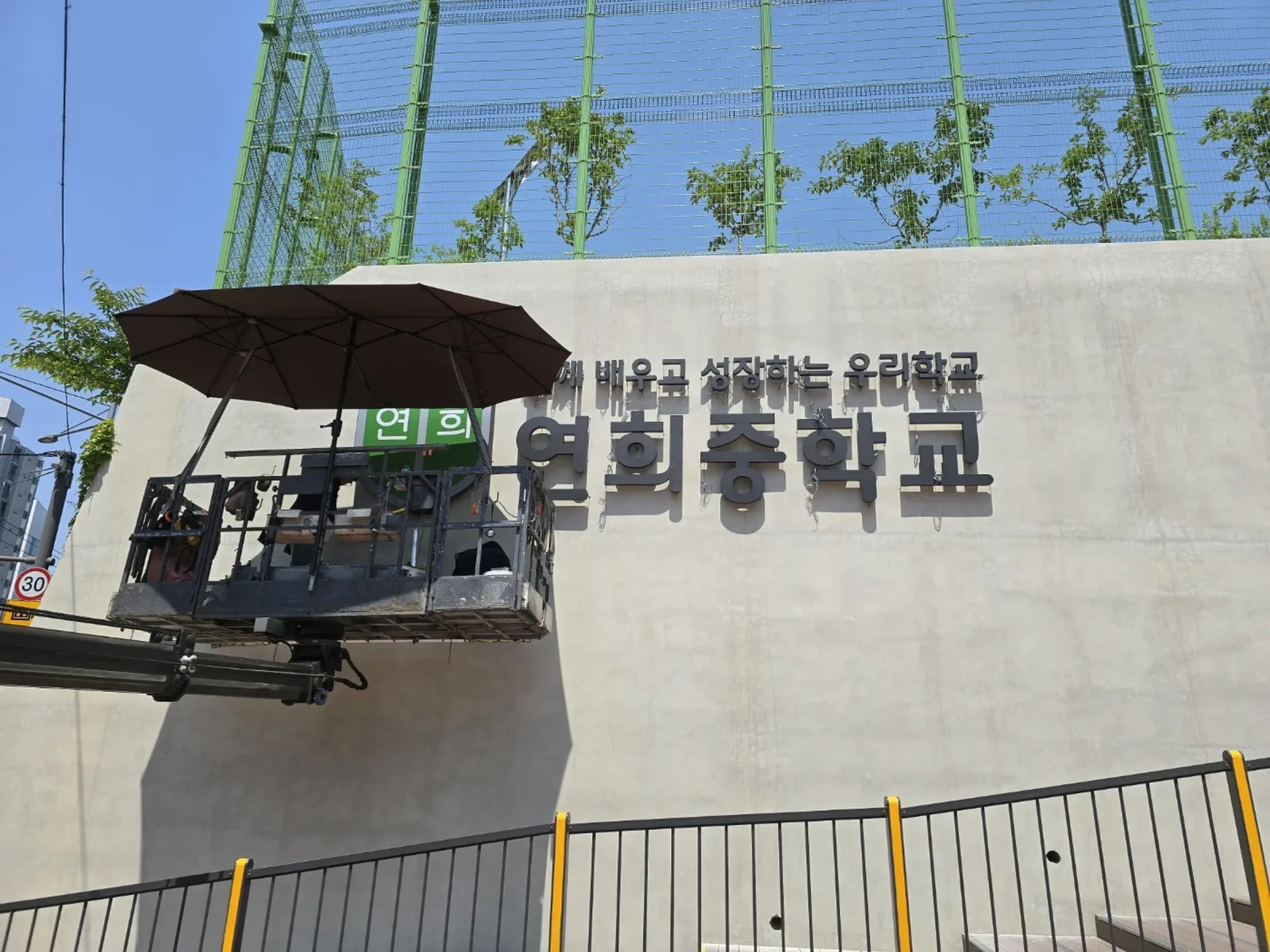 중학교 건물 외벽에 설치 완료된 입체 채널 글자 간판, 고소작업대가 남아있는 현장